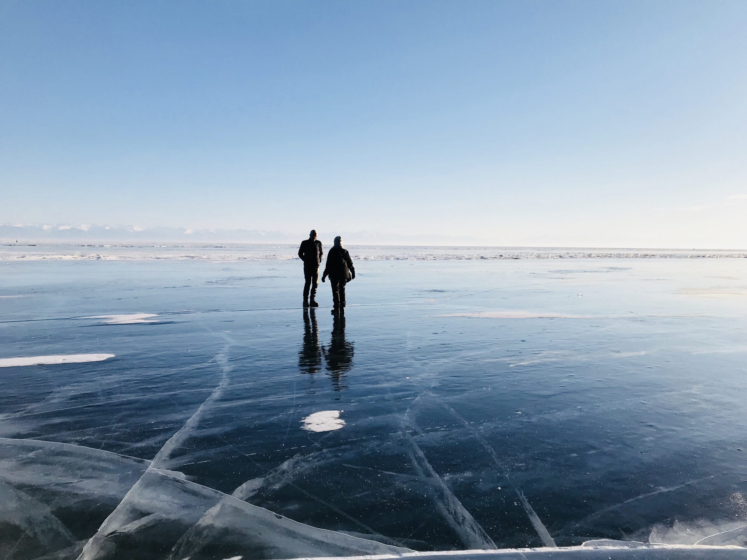 Fototour auf dem gefrorenen Baikalsee – zwei Teilnehmer:innen im goldenen Abendlicht auf weiter Eisfläche in Sibirien Teilnehmer einer Fototour auf dem gefrorenen Baikalsee in Sibirien bei Abendlicht – fotografisches Abenteuer im Winter mit Eislandschaft und goldener Stunde