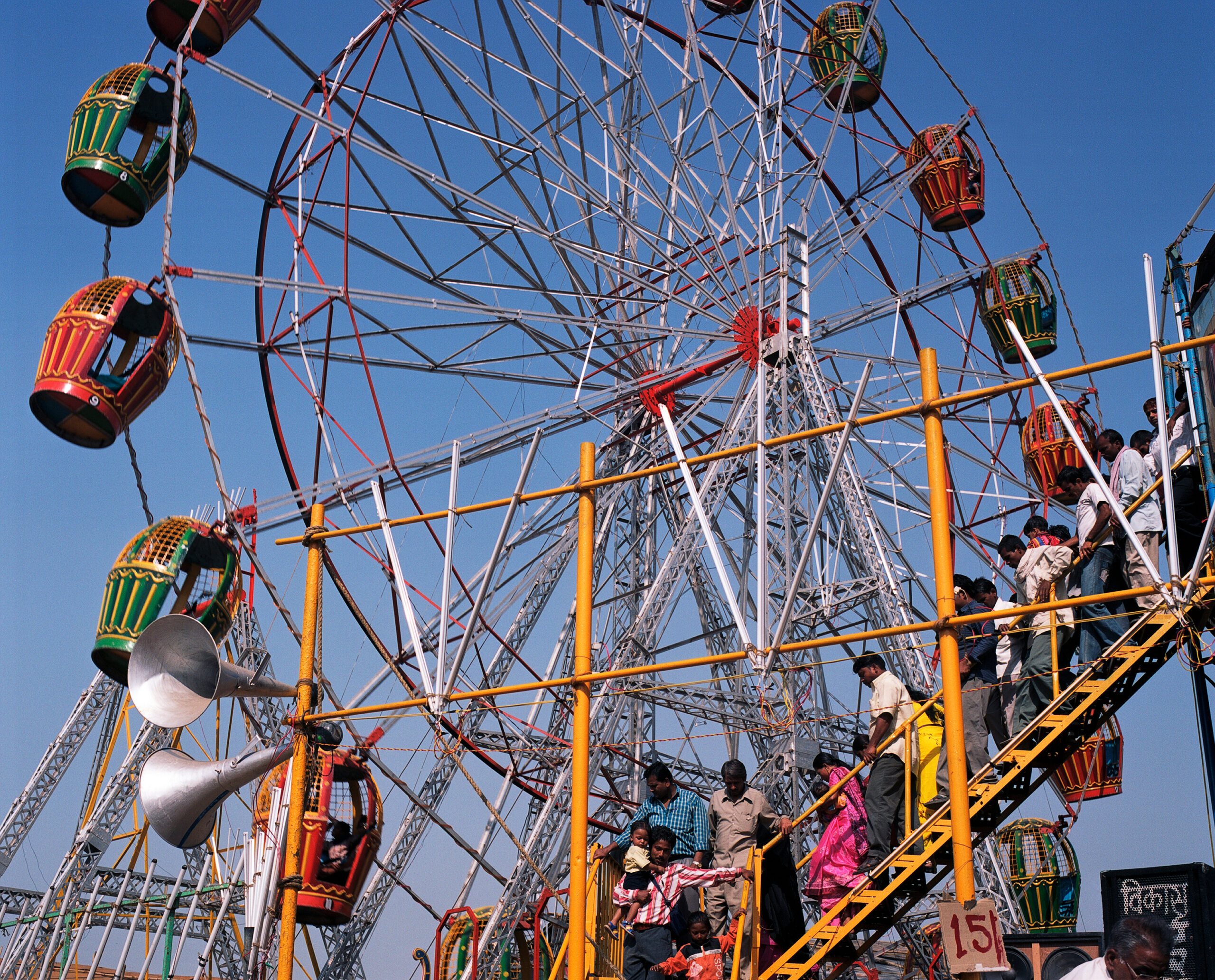 Buntes Riesenrad auf einer Festkirmes in Delhi – lebendige Farben während eines hinduistischen Feiertags Wärend einer Fotoreise in Indien: Farbenfrohes Riesenrad auf einer lebhaften Kirmes in Delhi während eines hinduistischen Festes. Menschen strömen, Musik liegt in der Luft. Die Szene zeigt die festliche Energie, Farbenpracht und Dynamik des indischen Alltagslebens.